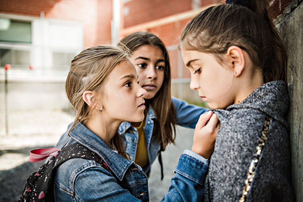 A girl sits alone against a brick wall, bullied – an image of how the HWDSB treated one parent who challenged compelled speech.
