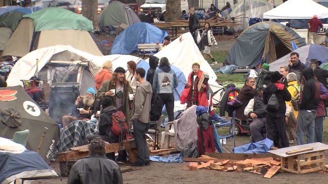 A Vancouver homeless camp is pictured with tents, open fire, and trash throughout a once-beloved park.